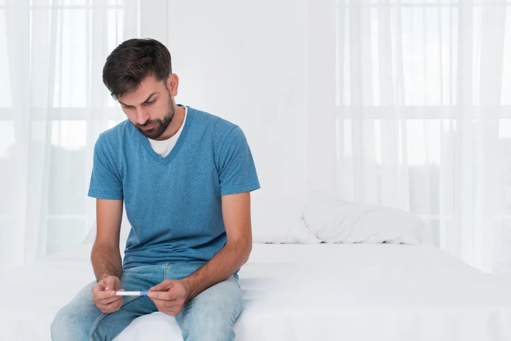 A man sitting on a bed looking at a pregnancy test